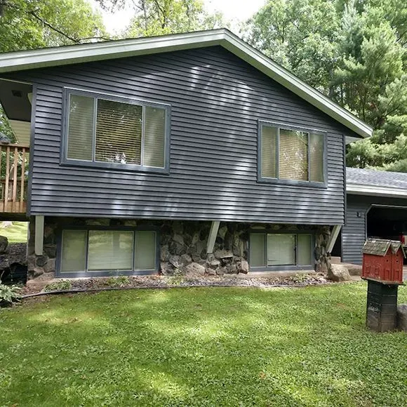 Completed full siding replacement with dark horizontal siding above a stone lower exterior