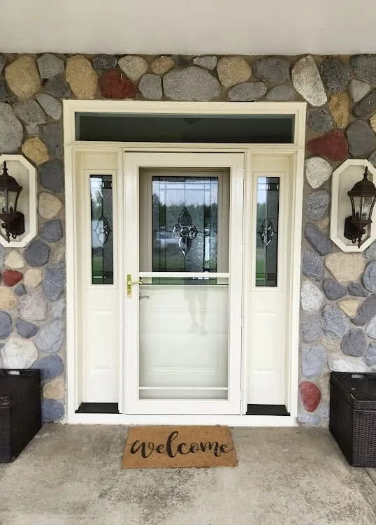 Completed white entry door replacement with decorative glass sidelights and transom on a stone exterior